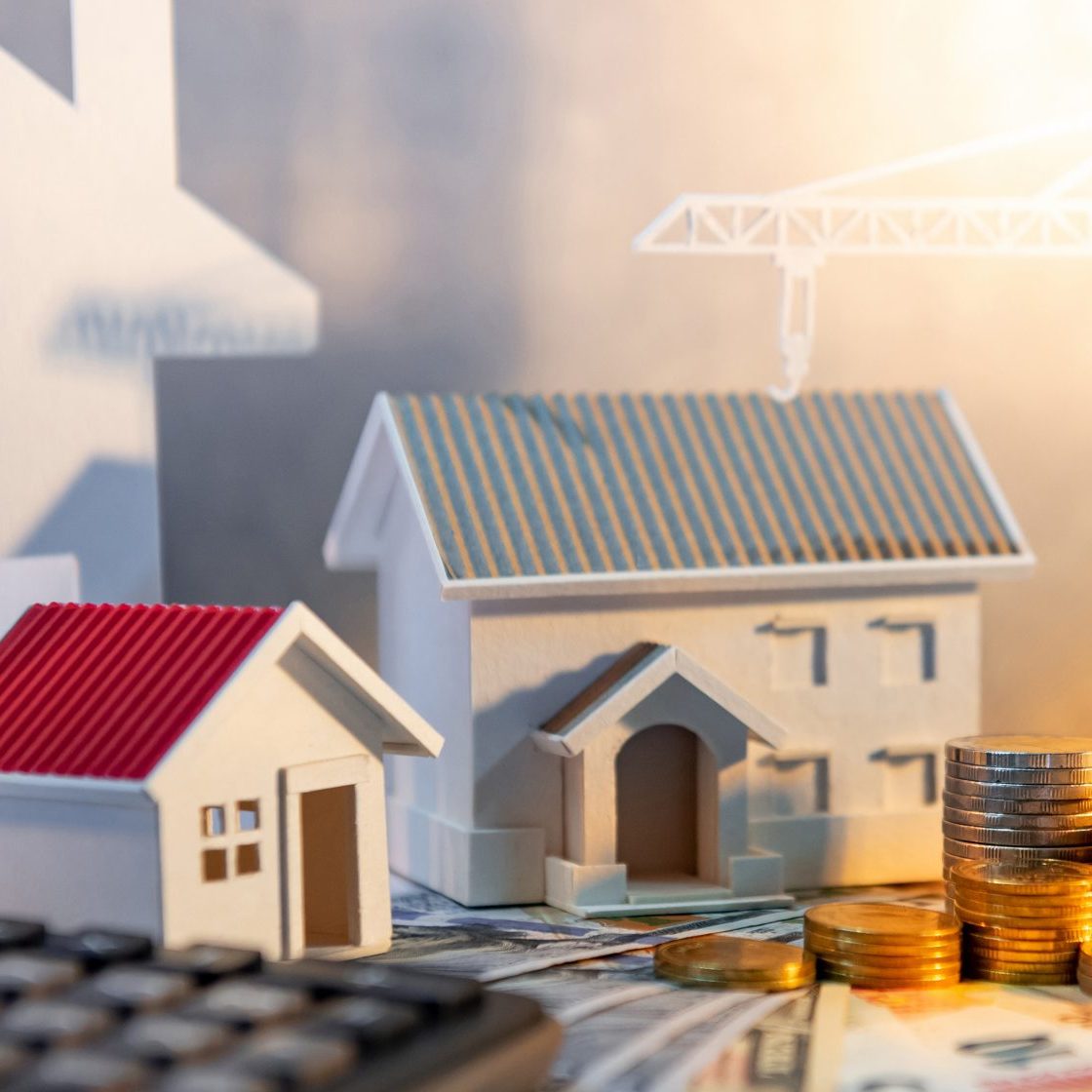 Real estate or property development. Construction business investment concept. Home mortgage loan rate. Coin stack on international banknotes with calculator, house and crane models on the table.