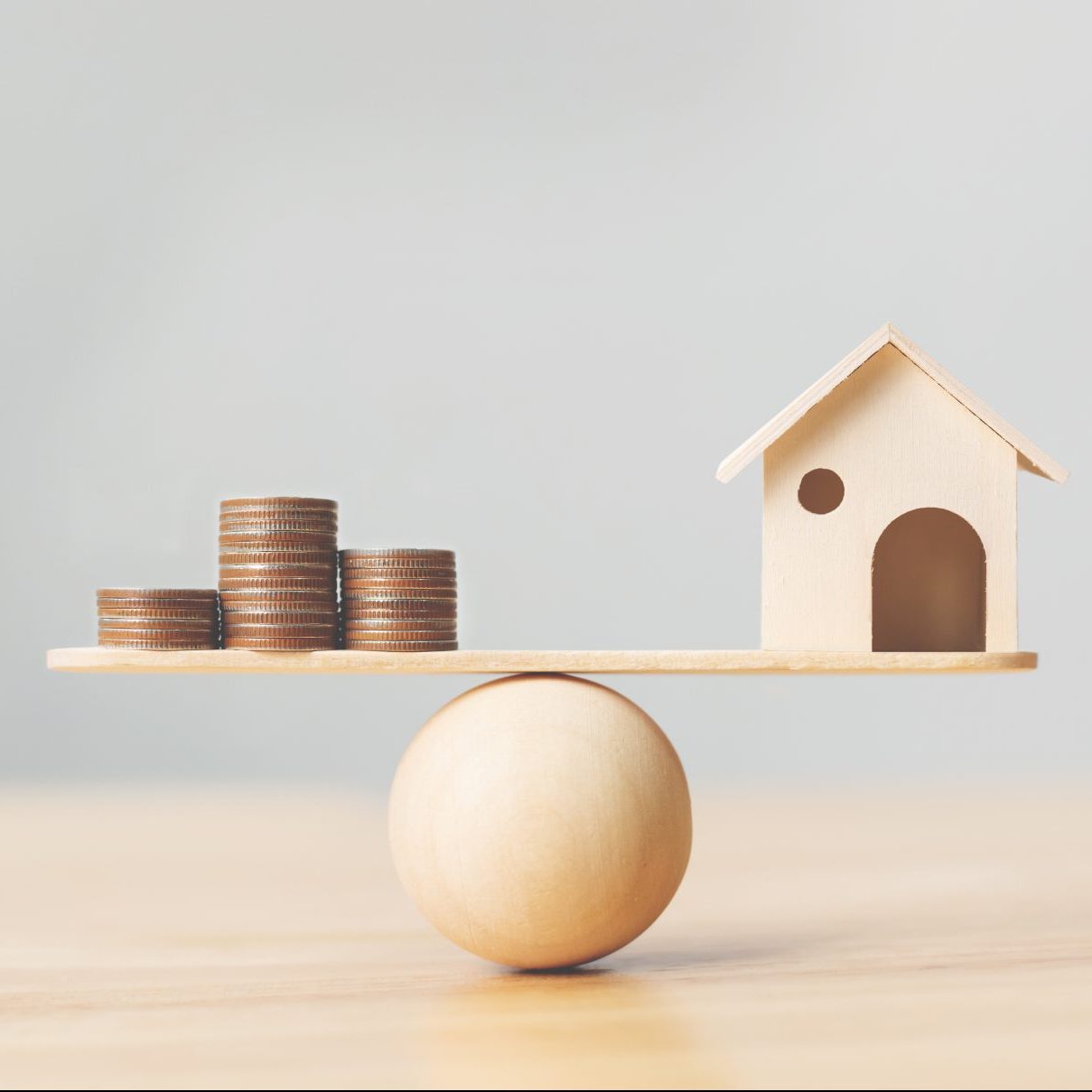 Wooden home and money coins stack on wood scale. Property investment and house mortgage financial real estate concept