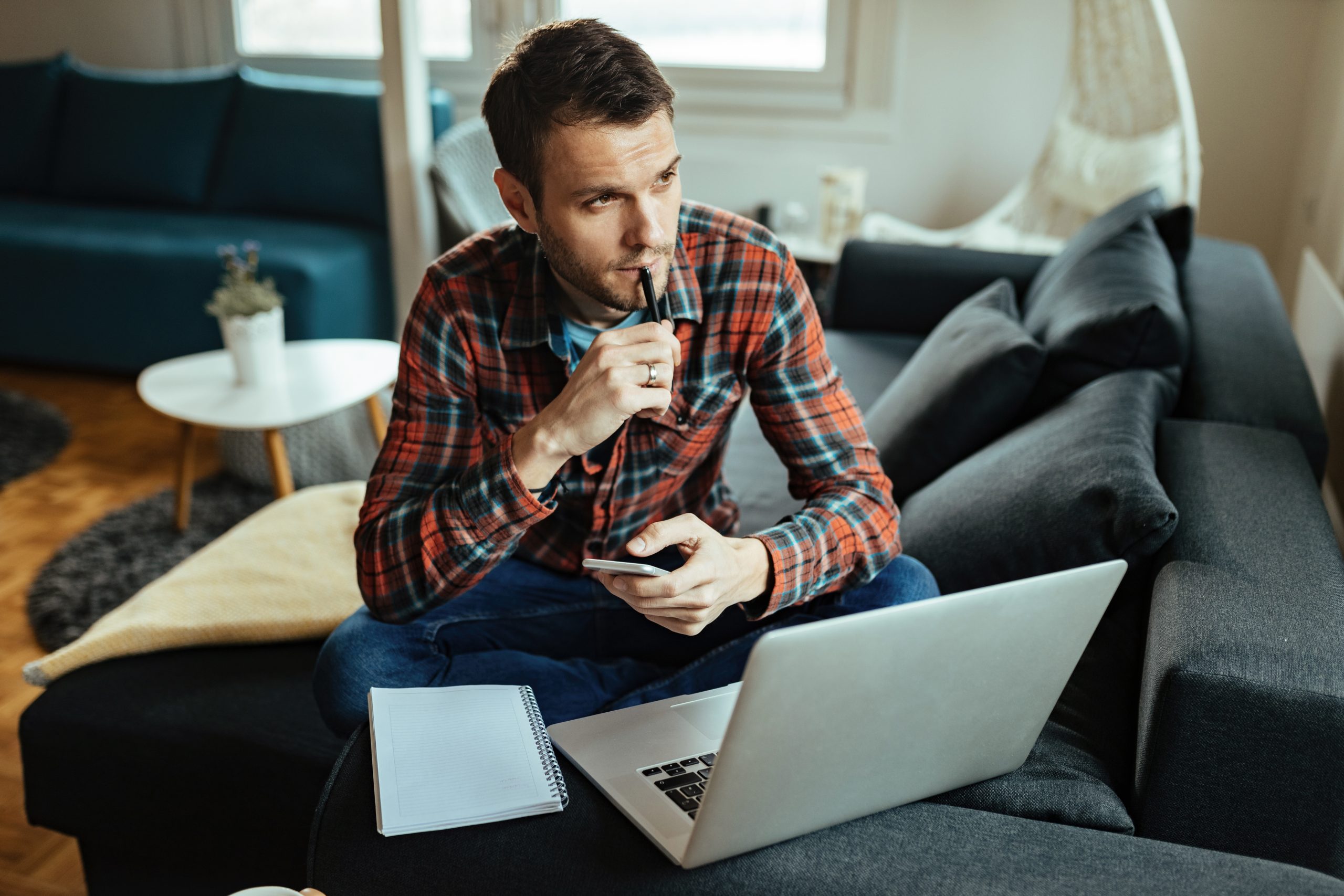 Thoughtful man using mobile phone and laptop while working at home.