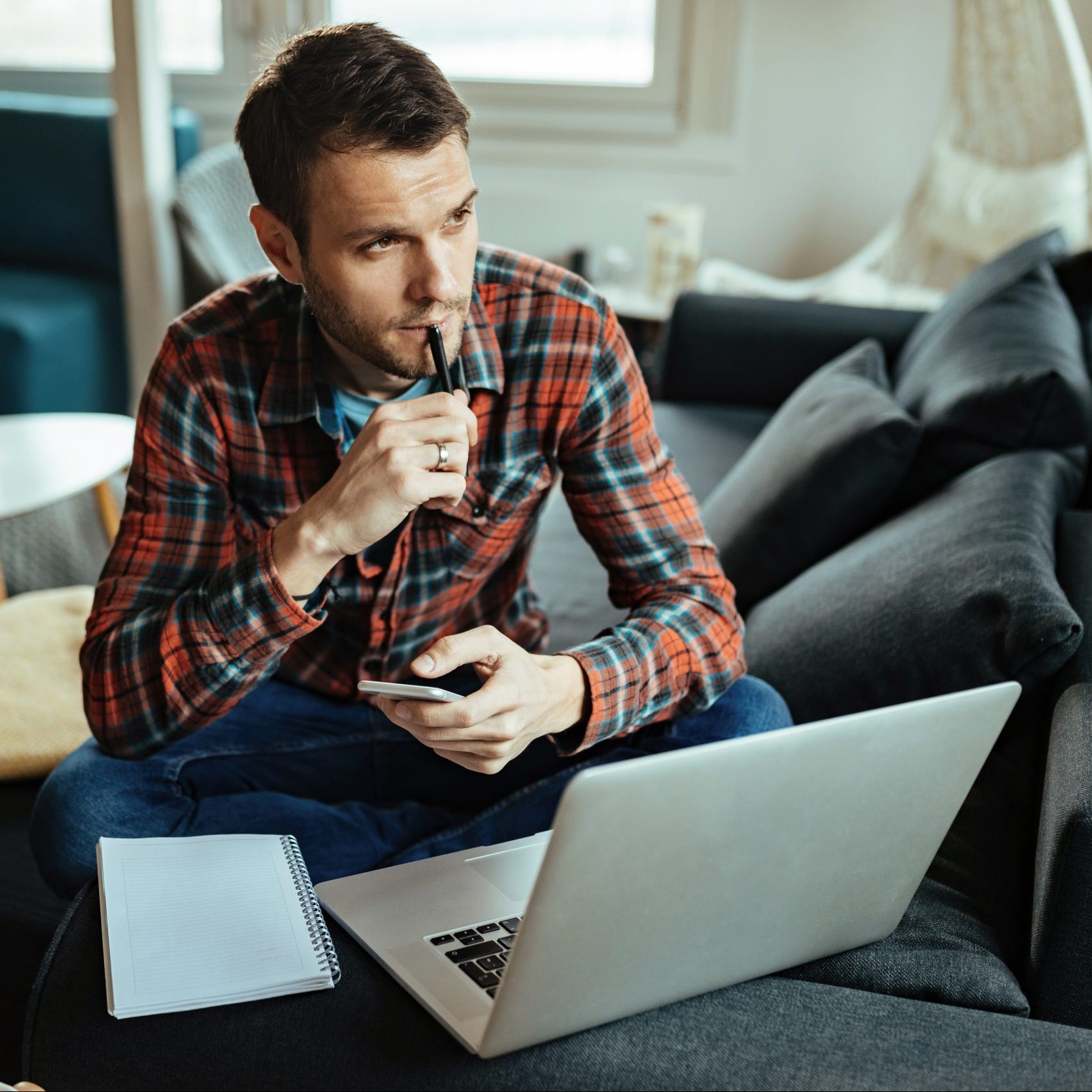 Thoughtful man using mobile phone and laptop while working at home.