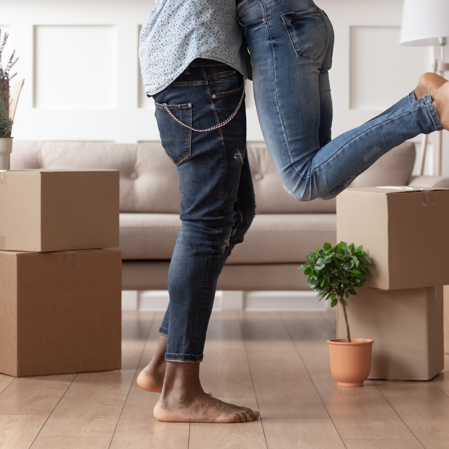Close up young husband in jeans lift wife surrounded by cardboard boxes excited to move in new flat, happy african American couple have fun hug feel euphoric relocating together to own house
